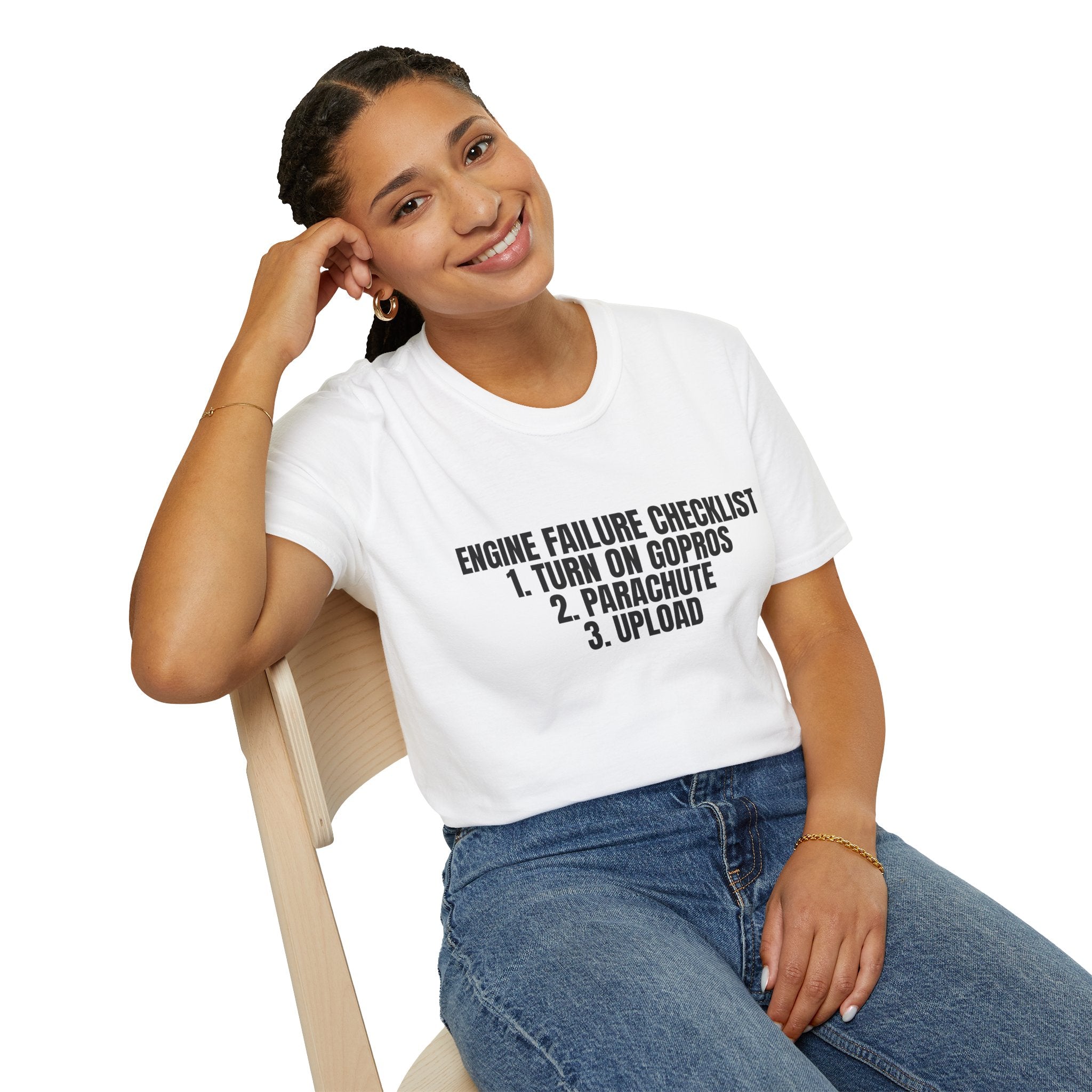 Person wearing a white t-shirt with humorous text design, sitting on a chair.